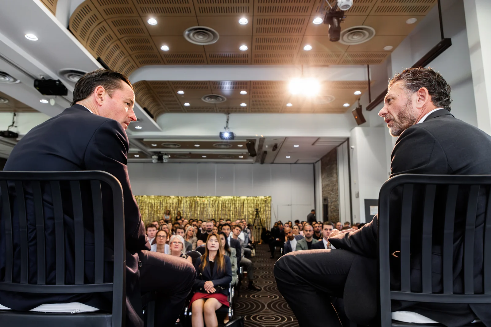 Two speakers in conversation, viewed from the stage toward the audience.