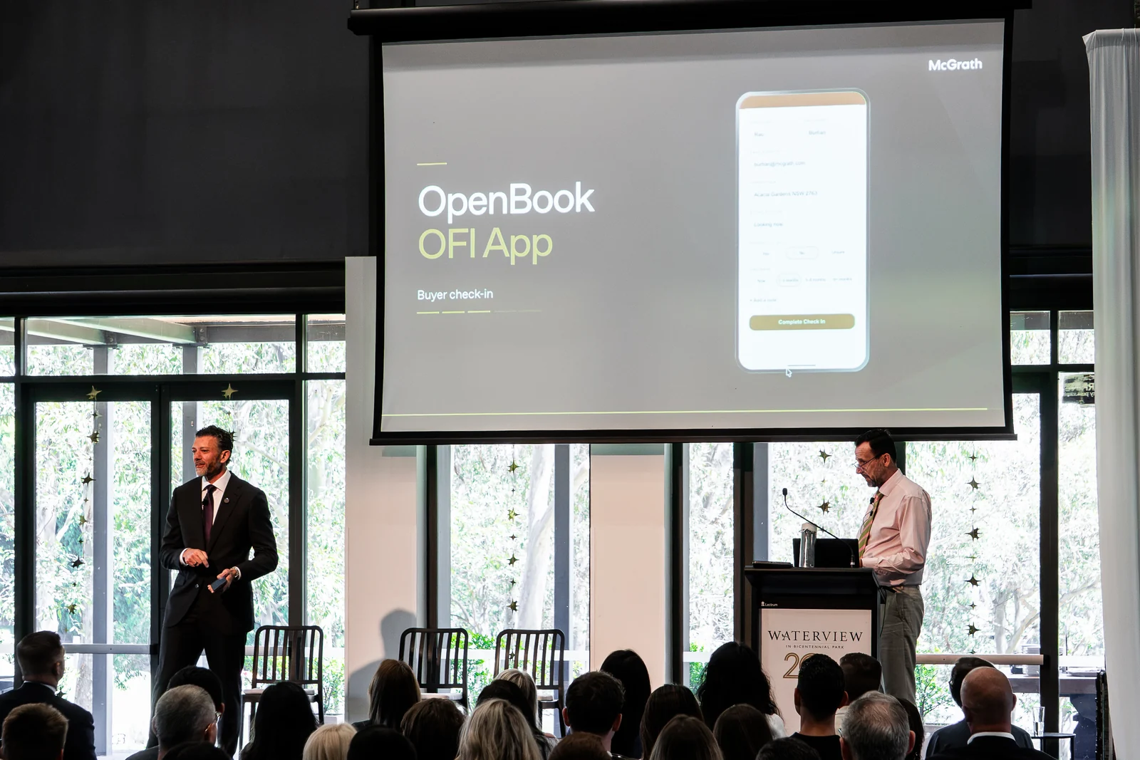 Speakers present an app demonstration to the seated audience.